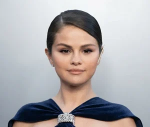Selena Gomez wearing a navy blue velvet halter gown with a crystal brooch detail and sleek low bun at a red carpet event
